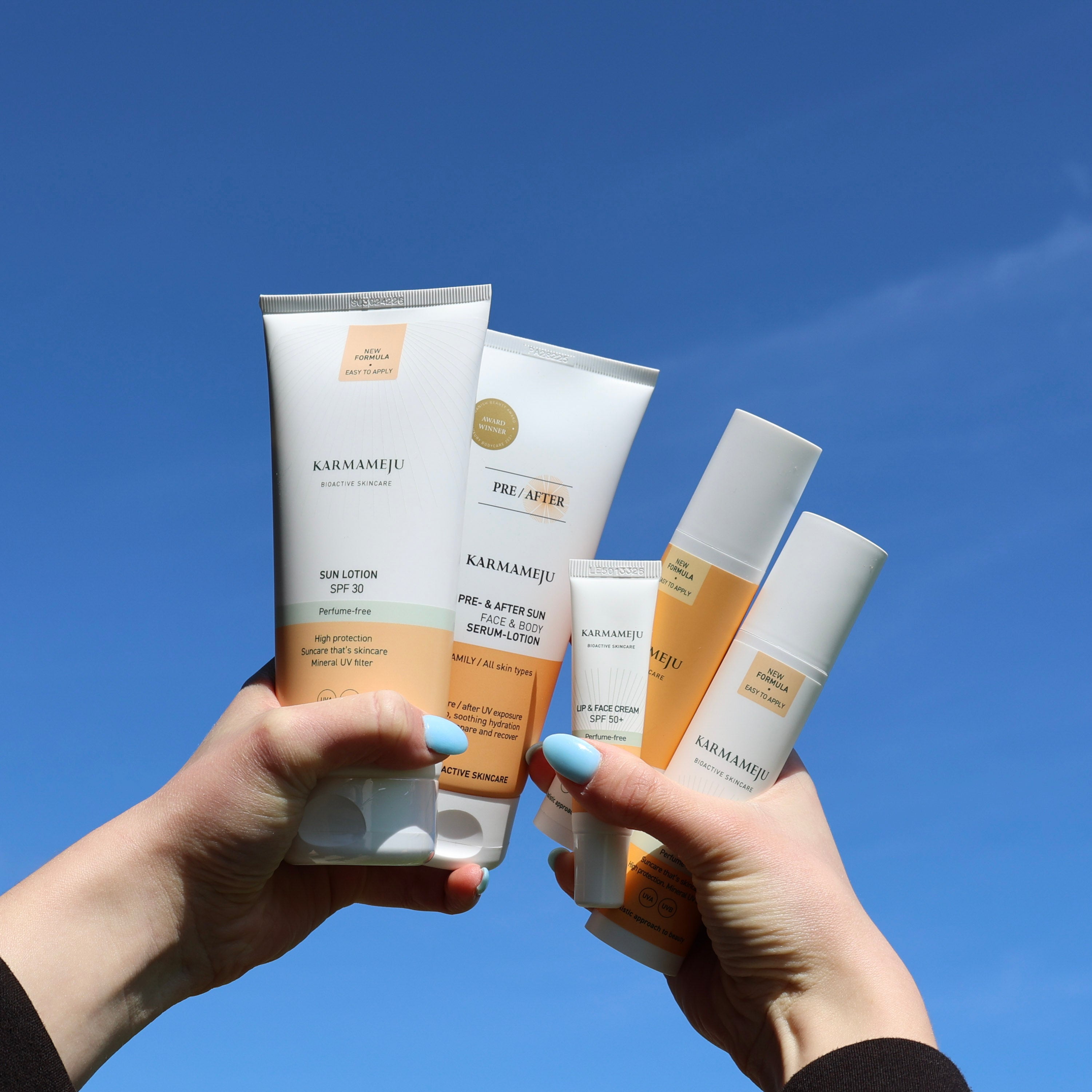 Karmameju solcreme og hudplejeprodukter holdt op mod en blå himmel